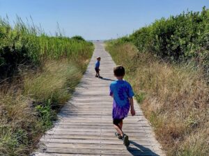 two young boys running down a wooden path between dunes